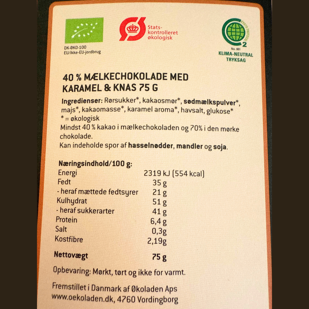 Bagsideetiket af Elmelund økologisk mælkechokolade med karamel og knas, inklusiv ingrediensliste og næringsindhold.