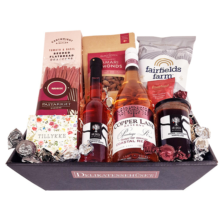 Gavekurv med ros&eacute;vin, delikatesser og et tillykke kort p&aring; en hvid baggrund.