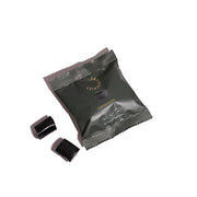 Grøn pose med saltlakrids fra Lakridseriet og to sorte lakridsstykker på hvid baggrund.