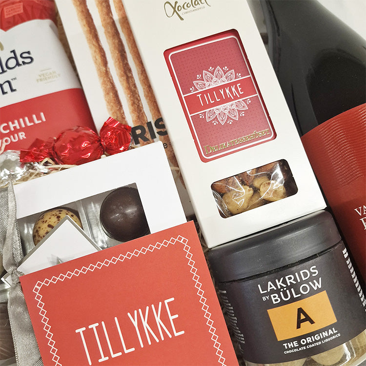 Nærbillede af gavekurv med rød tillykke tema indeholdende chokolade, lakrids og delikatesser fra Delikatessehuset.