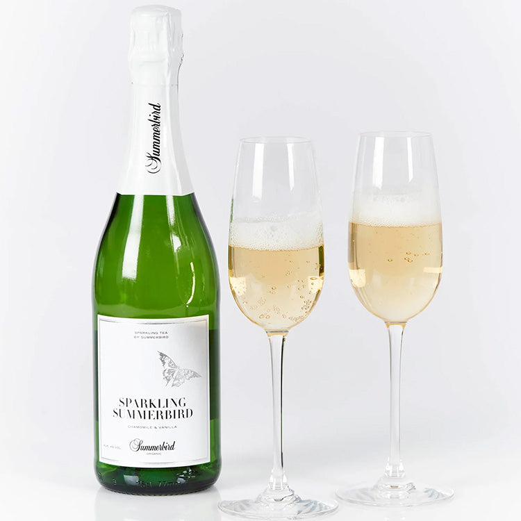 Flaske med Sparkling Summerbird te og to fyldte glas med bobler på hvid baggrund.