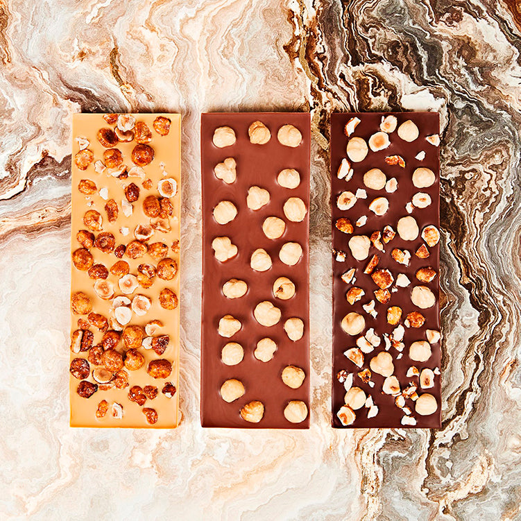 Tre forskellige Summerbird økologiske chokoladebarer med hele hasselnødder på en marmoreret baggrund.